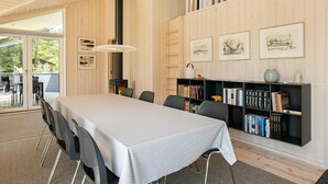 Et moderne spiseområde med et langt bord, stole, en bogreol og indrammede kunstværker på væggene.