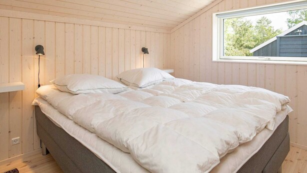 Et soveværelse med en seng, to sengeborde med lamper, et vindue og udsigt til et hus.
