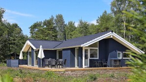 En moderne hytte med mørkeblå facade, store vinduer og en overdækket terrasse med havemøbler.