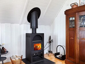 Una habitación con un horno de leña de madera oscura, un mueble de madera con puertas de cristal y una cesta de mimbre llena de leños.