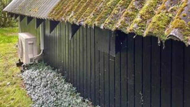 Un abri en bois, avec un toit recouvert de mousse et une petite construction attenante.
