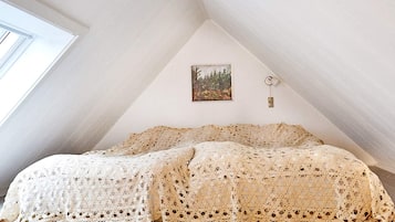 A bedroom with a sloped ceiling, a bed with a lace bedspread, a painting on the wall, and a nightlight.