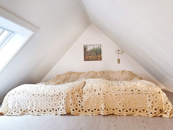 Un dormitorio con techo inclinado, una cama con colcha de encaje, un cuadro en la pared y una luz nocturna.