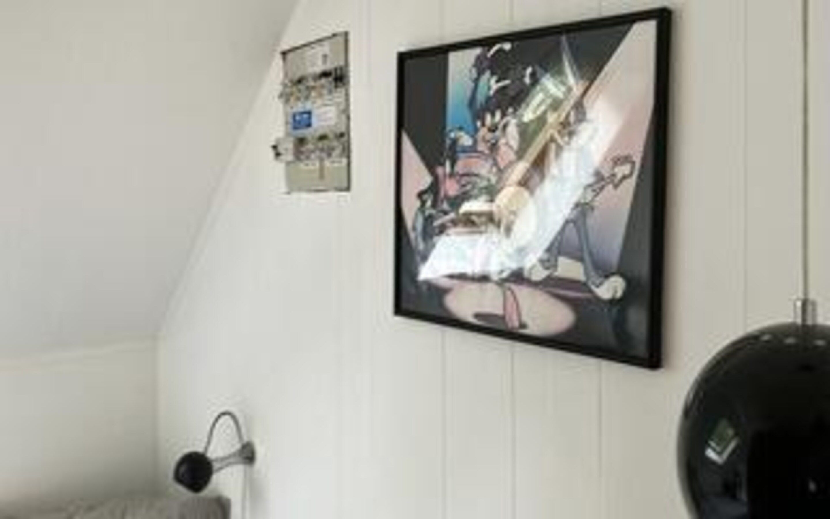 Una habitación con una obra de arte enmarcada en la pared, un objeto esférico negro y una pared blanca.