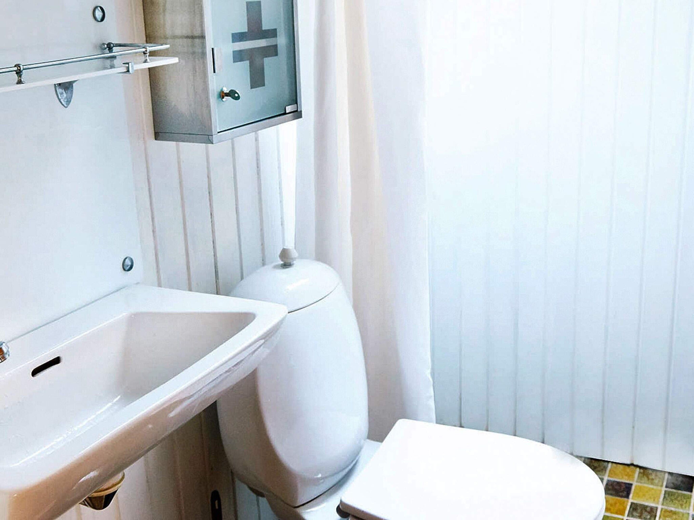 A bathroom with a white sink, a toilet, and a cabinet with a cross symbol.