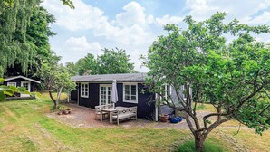 Et lille, mørkt hus med en veranda og et bord med stole.