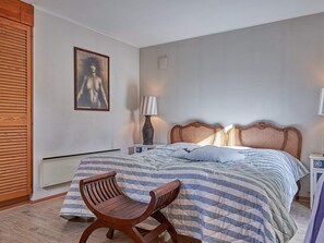 A bedroom with a bed, a wooden chair, a bedside table with a lamp, and a framed picture on the wall.