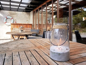 An outdoor patio with a wooden table, wicker chairs, a glass candle holder with a lit candle, and a lifebuoy on the wall. - Holiday Home in NexÃ¸ (Nexø)