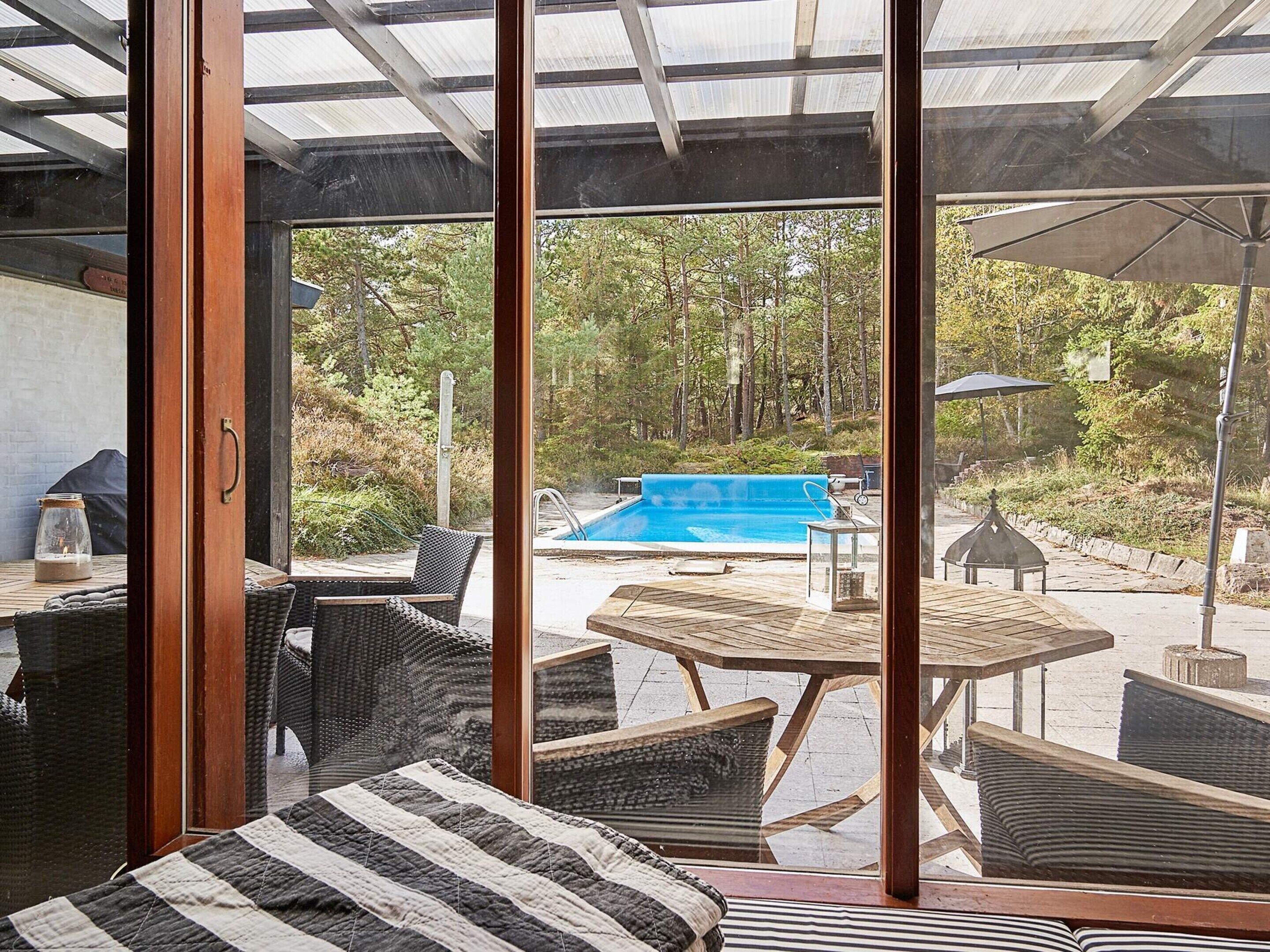 Una habitación con un gran ventanal, muebles de mimbre, piscina y un pabellón.