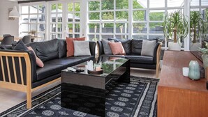 Una sala de estar moderna con un sofá modular, una mesa de centro de vidrio y ventanas amplias que ofrecen vista a la vegetación.