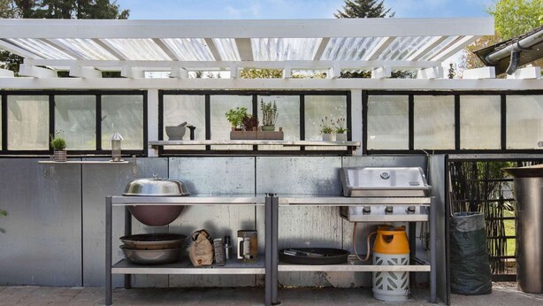 Una cocina con una parrilla, un lavamanos y un estante con distintos utensilios de cocina.