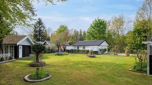 Una propiedad residencial con un césped cuidado, un pequeño jardín con un árbol y una casa blanca con techo oscuro.