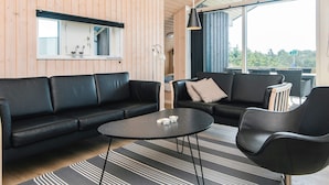 A modern living room with a black leather sofa, a round coffee table, and a black armchair. There is a large window providing a view of the outdoors.
