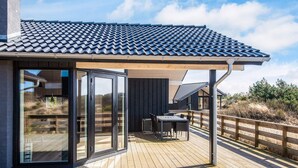 A modern house with a tiled roof, a wooden deck, and a glass door leading to a patio area.