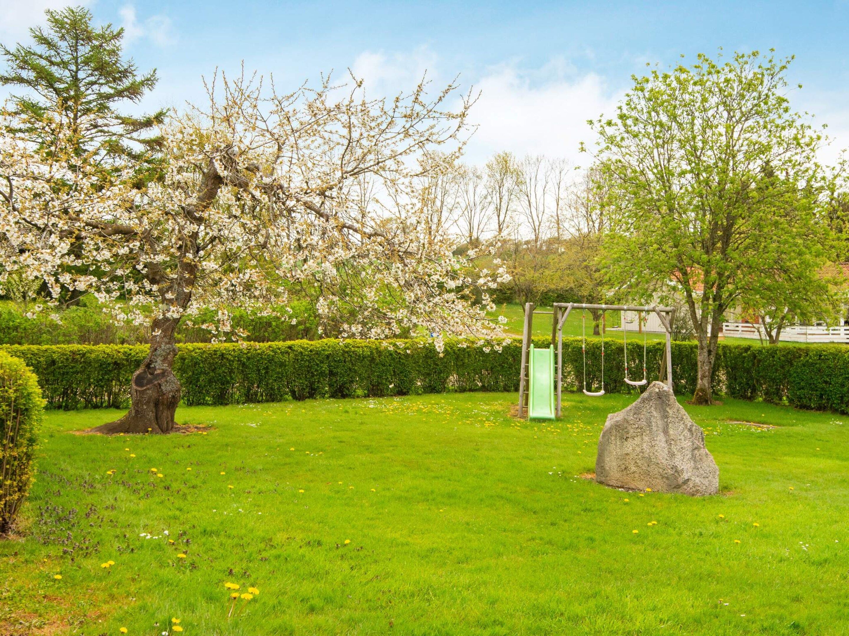 A park with a grassy area, a playground with a swing set, and a large rock.