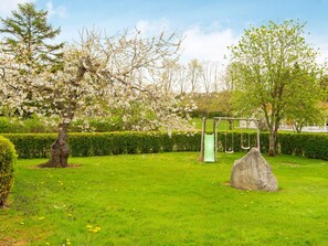 A park with a grassy area, a playground with a swing set, and a large rock. - 6 Person Holiday Home in Hejls (Hejls)