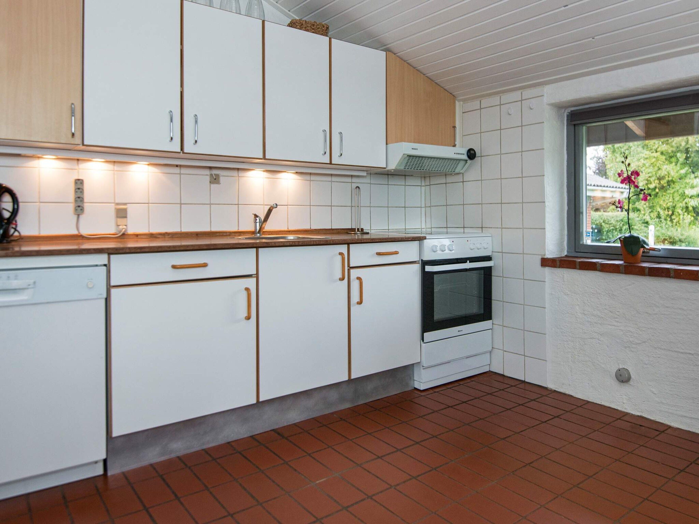 A kitchen with white cabinets, a stove, and a window with a view of greenery.