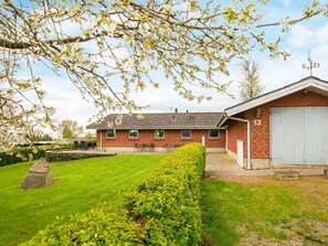 A brick building with a garage, a lawn, and a tree with white blossoms. - 6 Person Holiday Home in Hejls (Hejls)