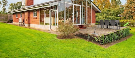 A modern house with a glass conservatory, a brick exterior, and a well-maintained lawn.