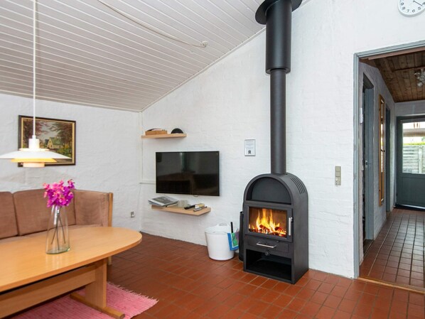 A living room with a fireplace, a TV mounted on the wall, a sofa, and a table with a vase of flowers. - 6 Person Holiday Home in Hejls (Hejls)