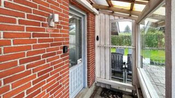Een bakstenen buitenmuur, een glazen deur en een overdekte veranda.