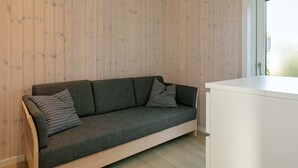 A modern room with a wooden panel wall, a grey sofa with patterned cushions, and a white cabinet. - Holiday Home in Sæby (Sæby)