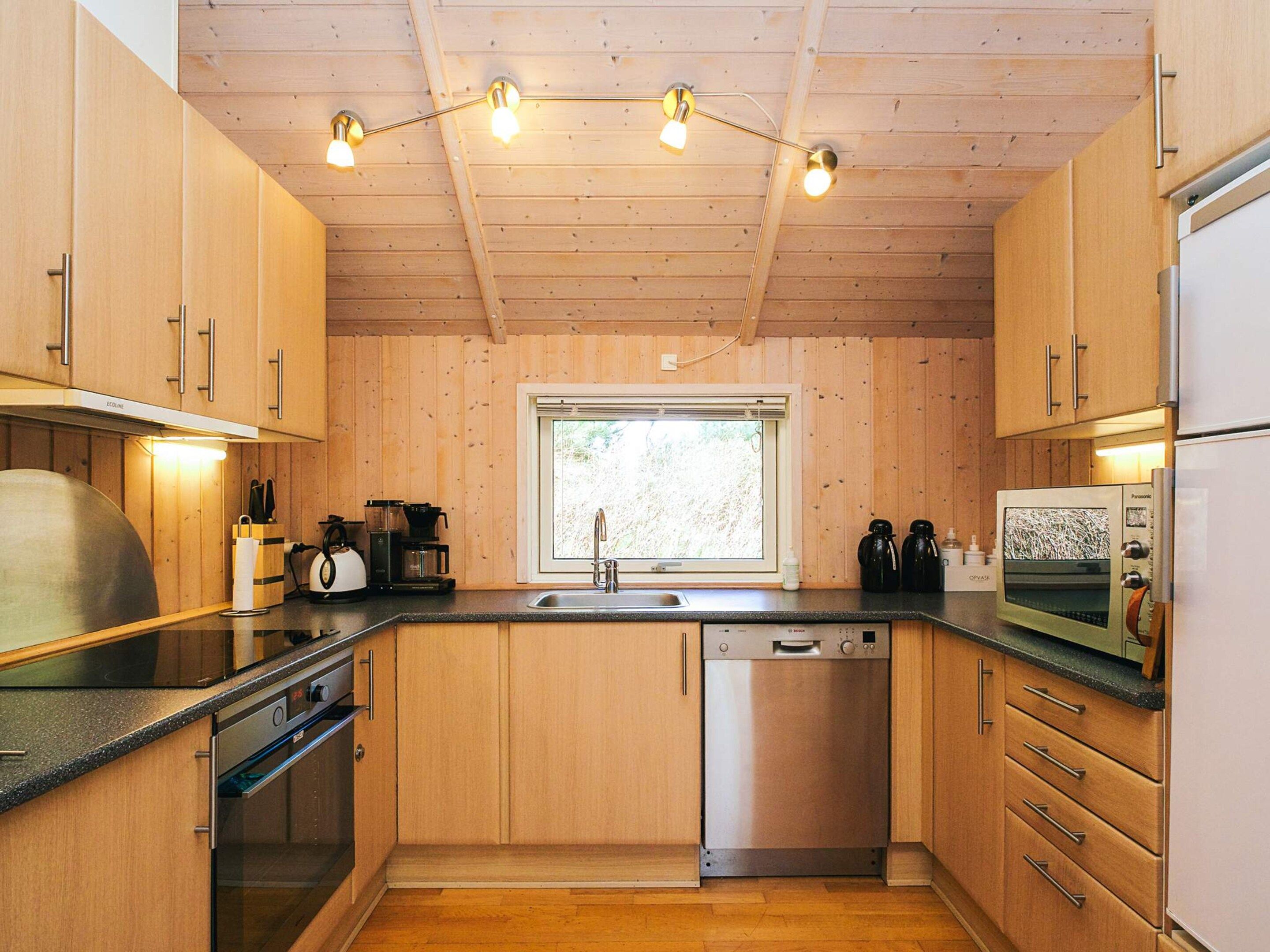 Una cocina compacta con armarios de madera, lavavajillas de acero inoxidable, microondas y cafetera.