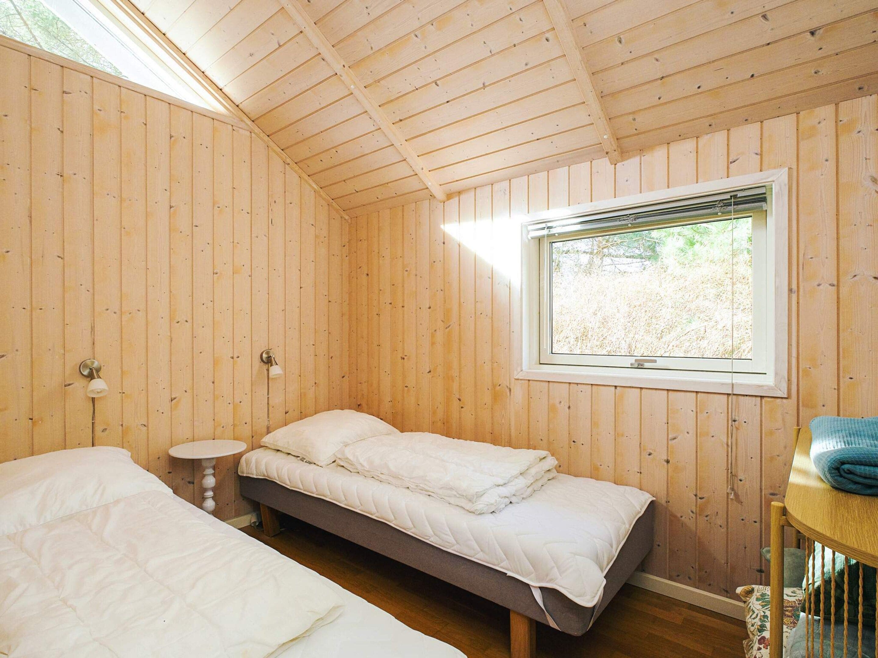 A wooden cabin room with two beds, a window, and a small table.