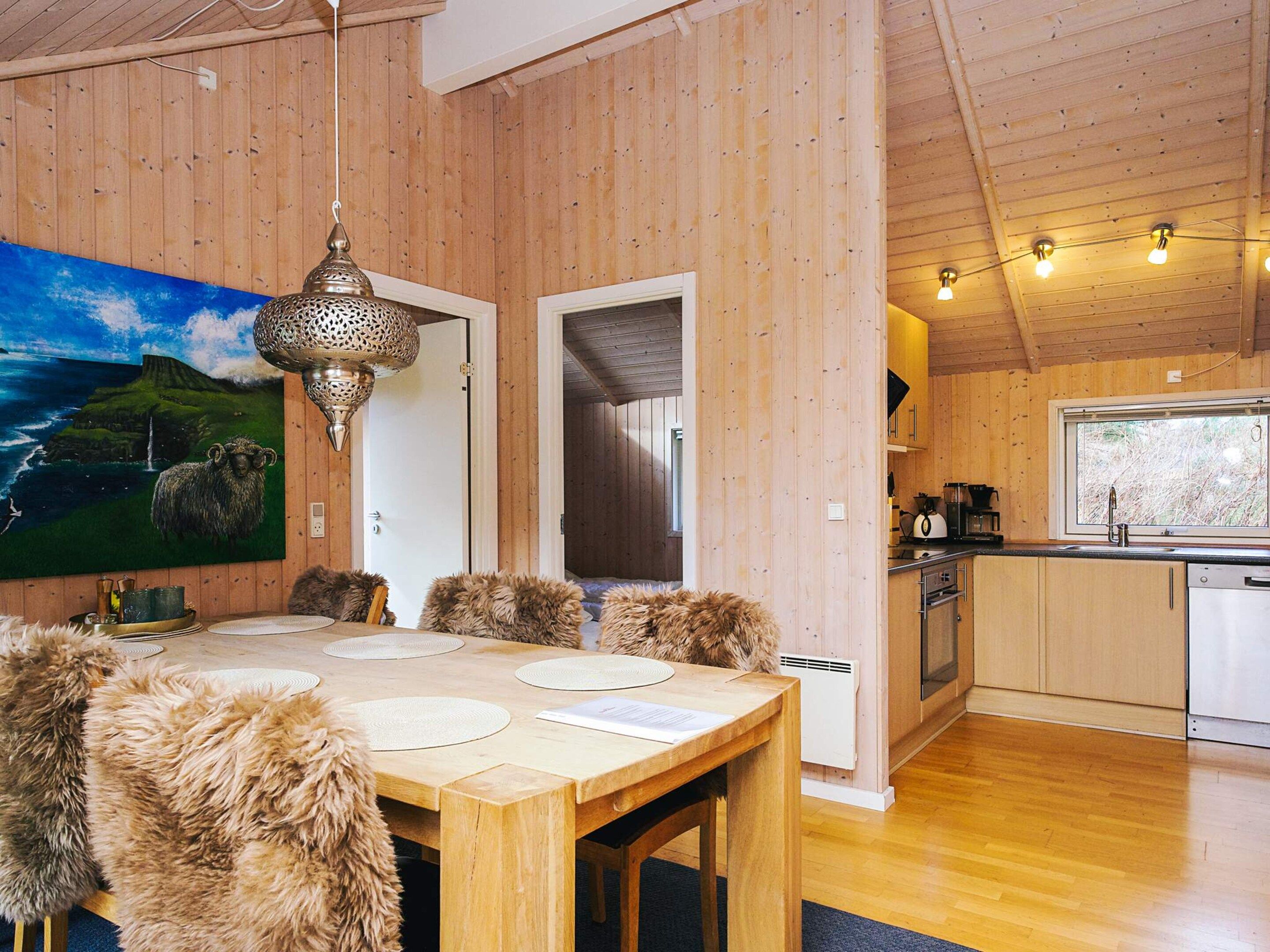 Un interior de madera con una mesa de comedor, sillas de piel, una cocina y un cuadro de un paisaje.
