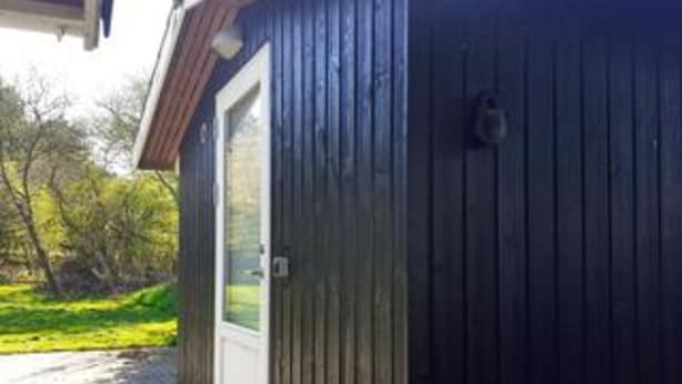 A wooden building with a white door, a small window, and a metal object on the wall. - Holiday Home in HÃ¸jby (Hojby)