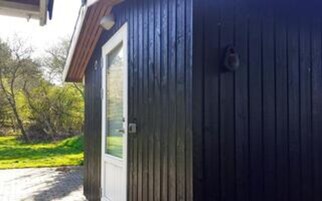 Un edificio de madera con una puerta blanca, una ventana pequeña y un objeto metálico en la pared.