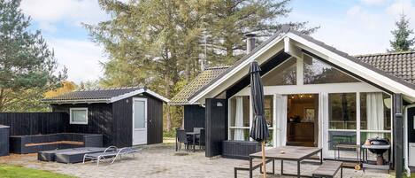 A modern outdoor patio with a dining table, chairs, and a grill area.