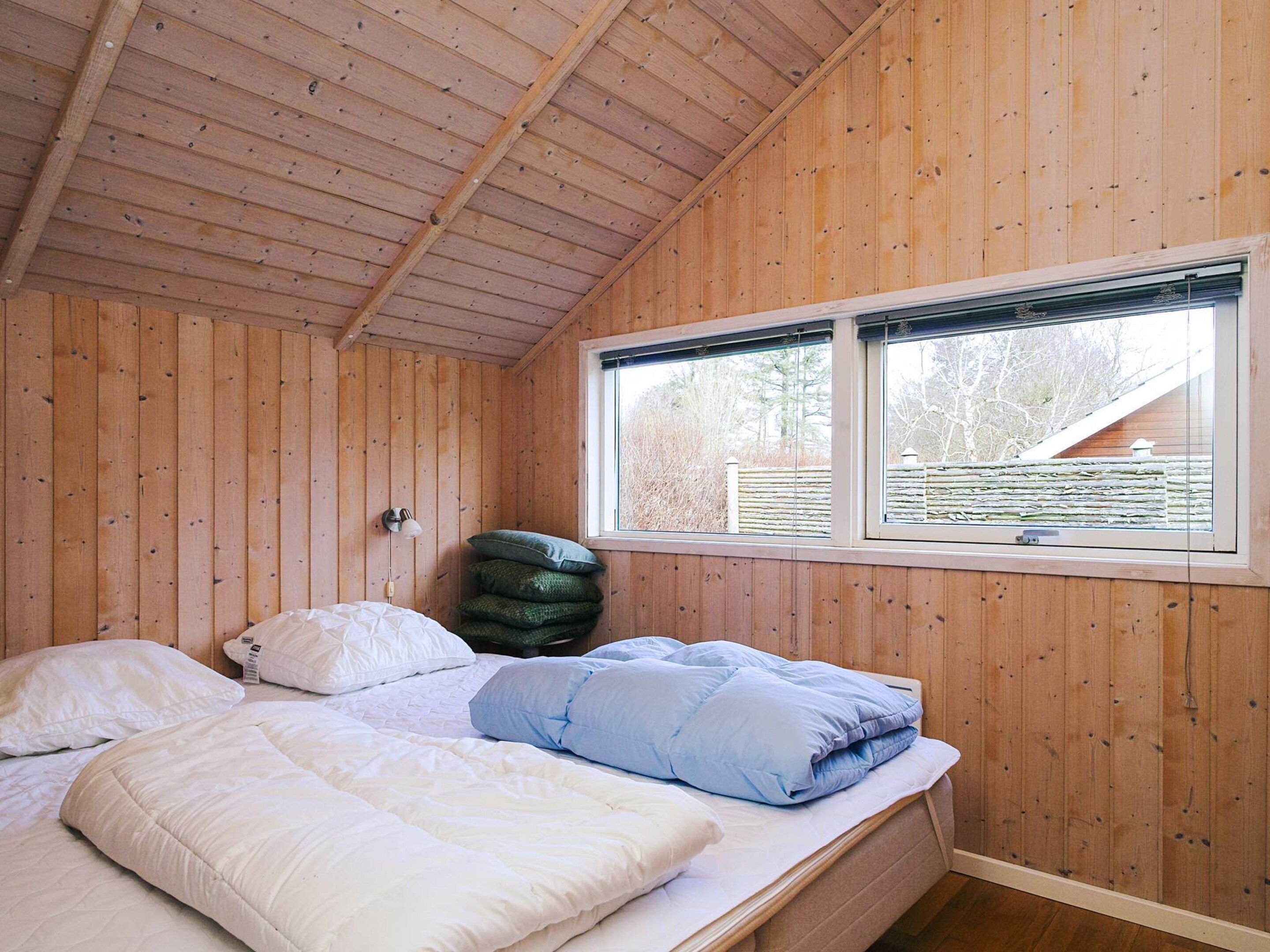 Una habitación con paneles de madera, una cama, almohadas, una ventana y una lámpara fijada a la pared.