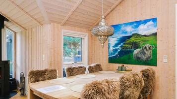 Interior de madera con una mesa de comedor, sillas de piel, una lámpara colgante y un cuadro de una oveja junto al mar.