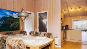A wooden interior with a dining area, a kitchen, and a large painting of a landscape.