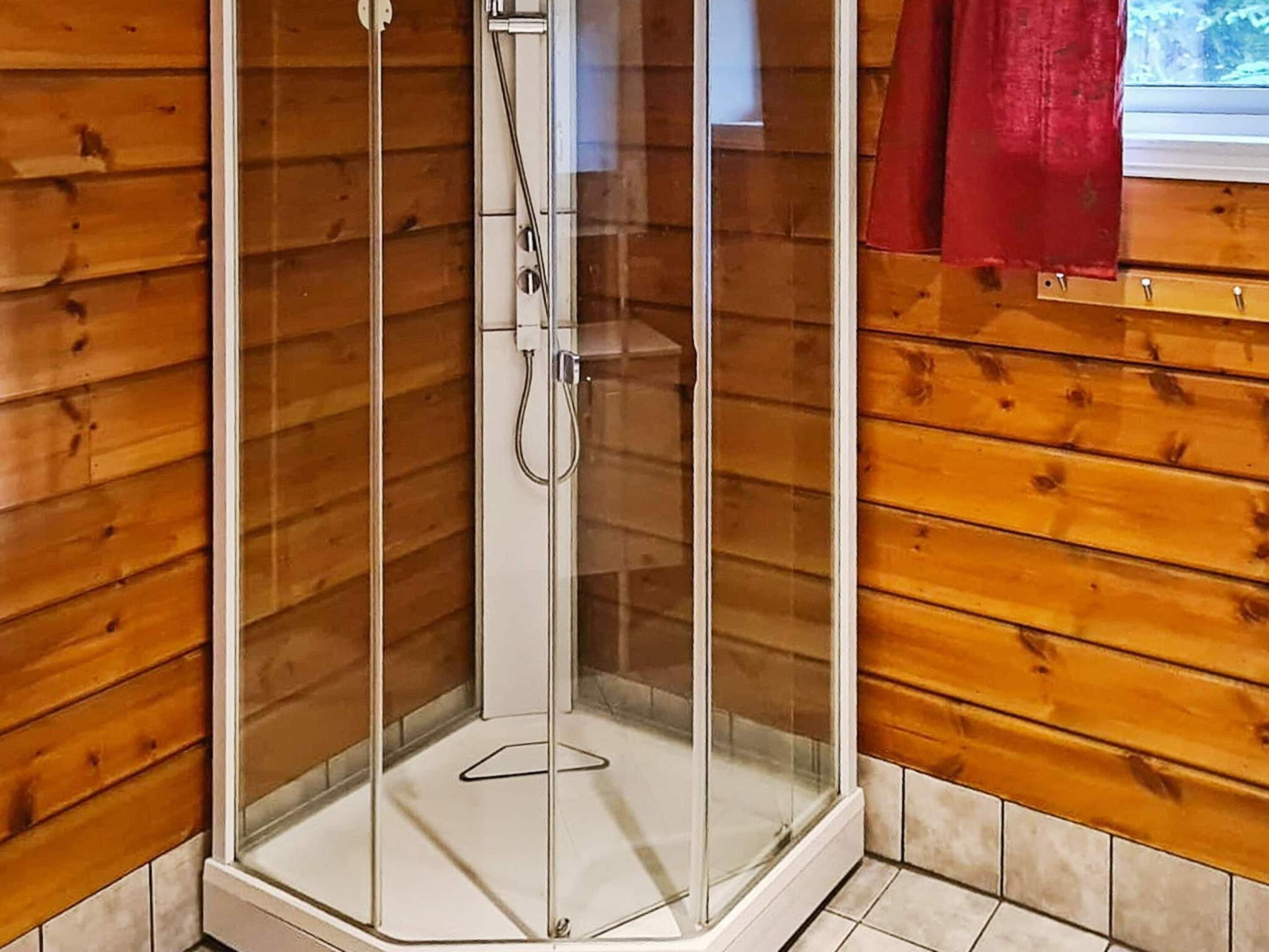 A glass-enclosed shower stall with a tiled floor, wooden walls, and a red curtain.