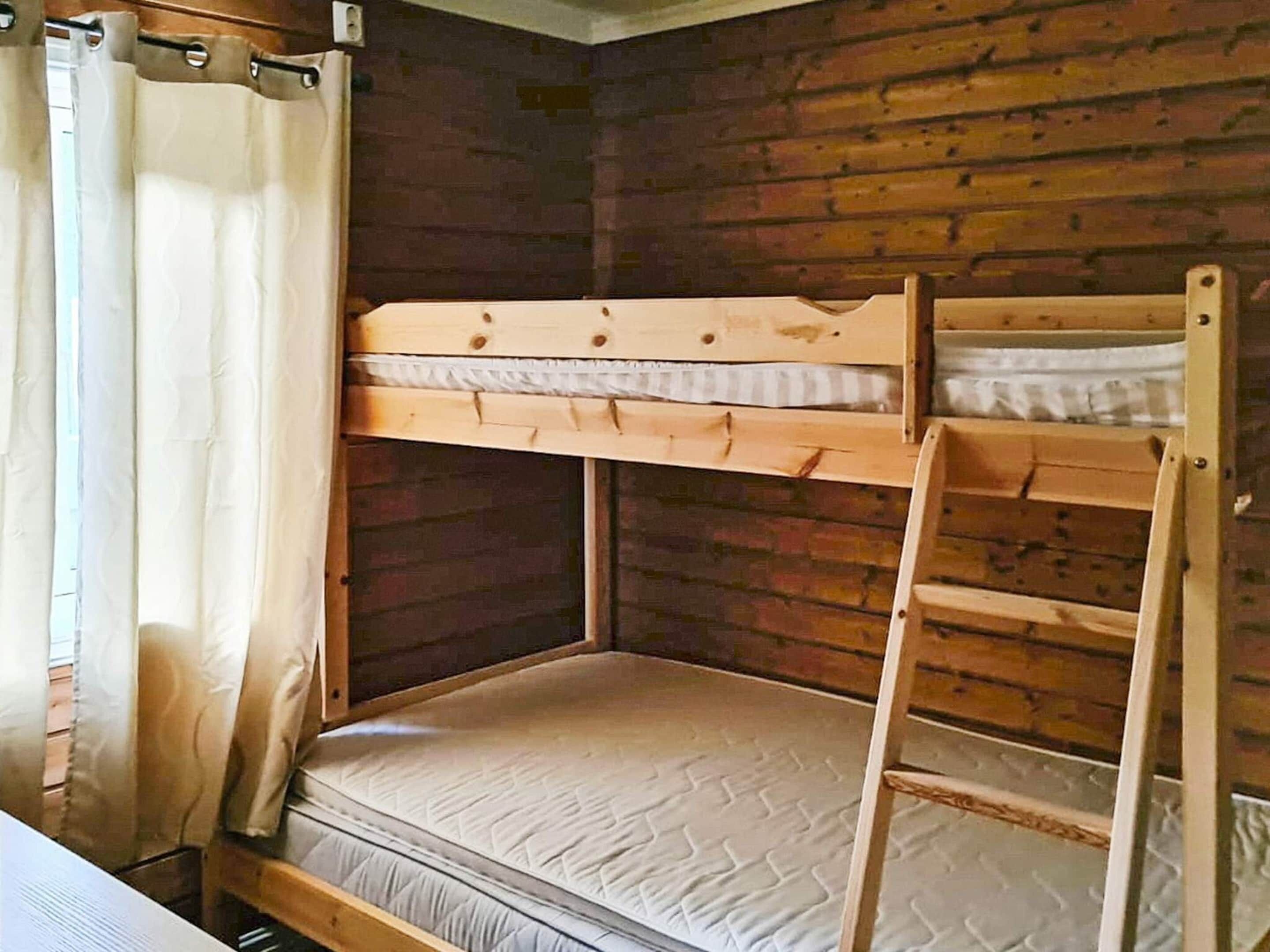 A bunk bed room with a wooden ladder and a window with curtains.