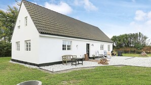 A white single-story house with a tiled roof, a front porch with a bench, and a small garden area with gravel and grass. - 6 Person Holiday Home in Lokken (Lokken)