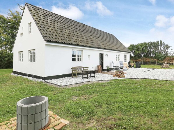 A white single-story house with a tiled roof, a front porch with a bench, and a small garden area with gravel and grass. - 6 Person Holiday Home in Lokken (Lokken)