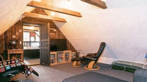 A cozy attic room with a sloped ceiling, a rocking chair, a cushioned bench, a television, and a bookshelf. - 6 Person Holiday Home in Lokken (Lokken)