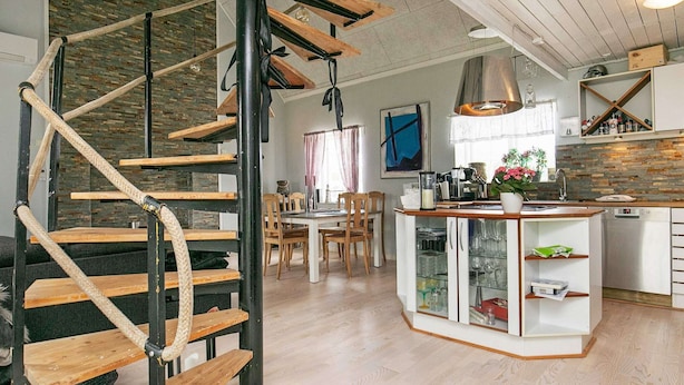 A modern kitchen with a central island, wooden staircase, and a dining area with chairs and a table. - 6 Person Holiday Home in Lokken (Lokken)