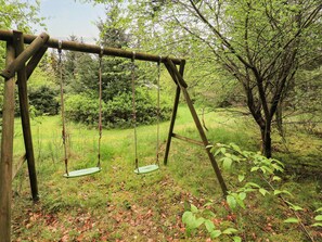 A wooden swing set in a wooded area with grass and trees.