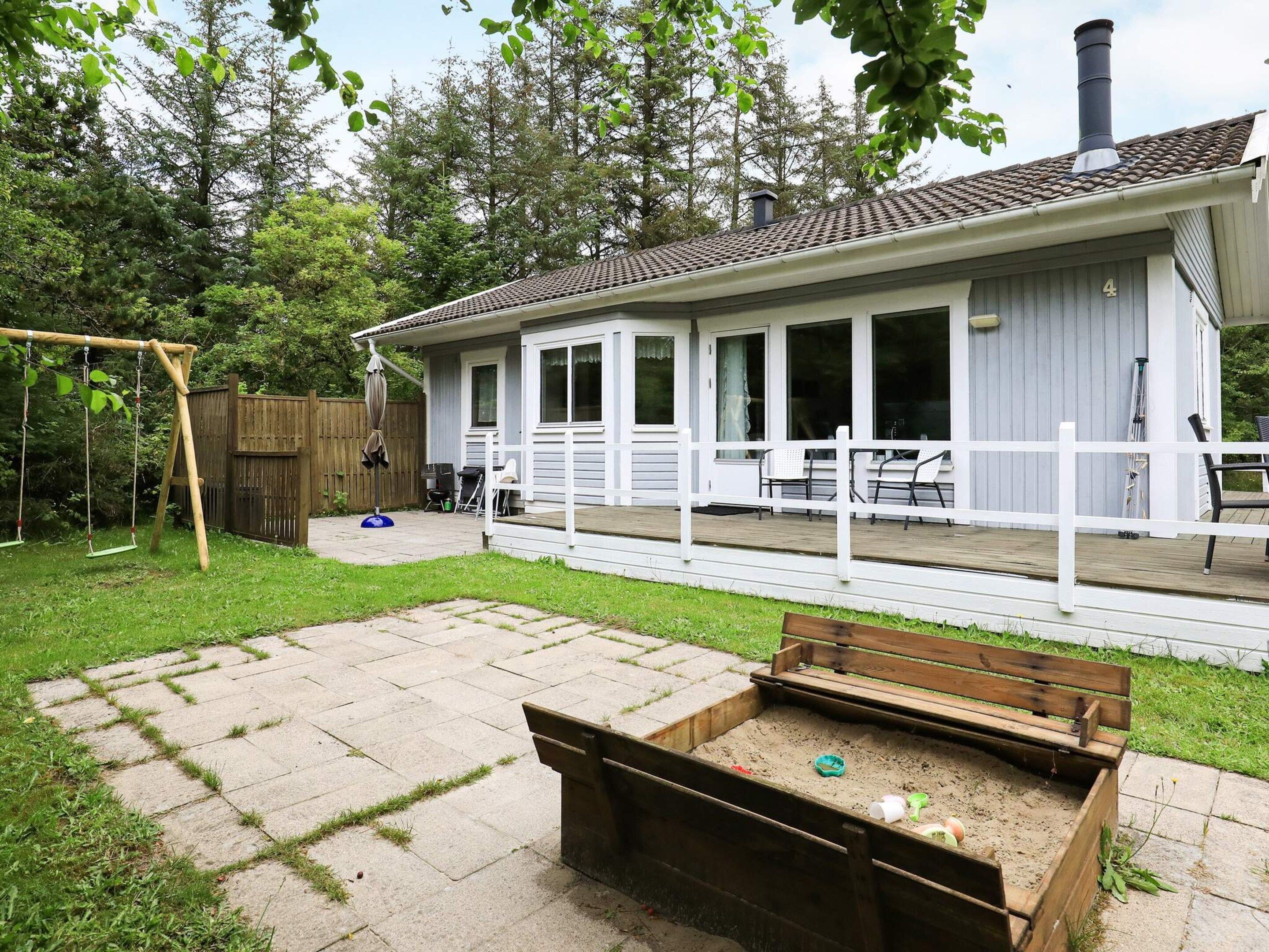 A house with a covered patio, a swing set, and a sandbox.