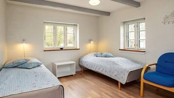 Una habitación con dos camas individuales, un pequeño tocador blanco, una silla azul y dos lámparas de pared.