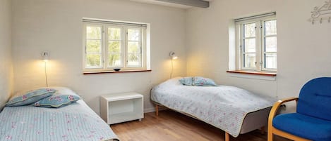 A room with two single beds, a small white nightstand, a blue chair, and two wall-mounted lights.