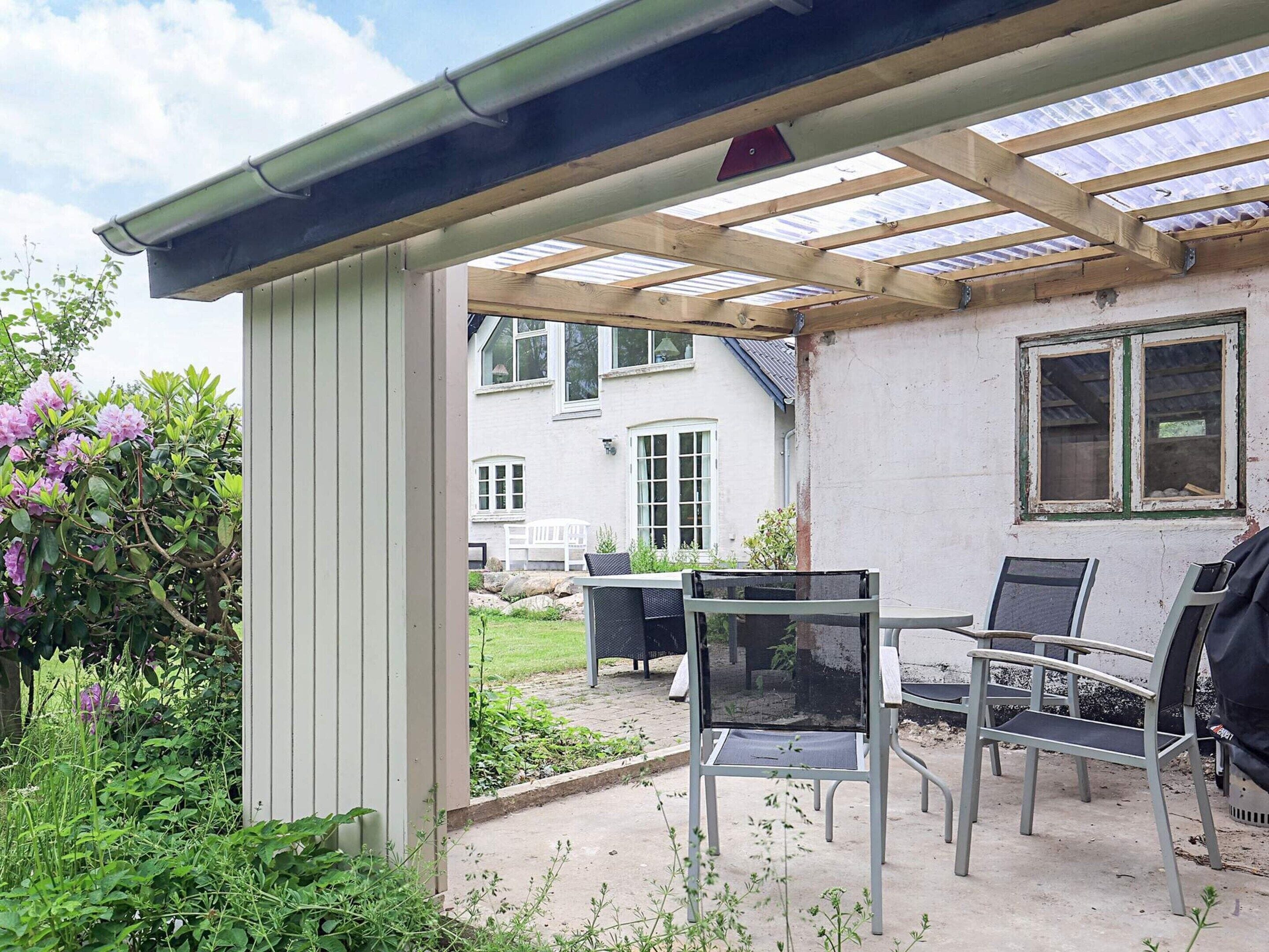 Un patio couvert avec une table et des chaises, un barbecue et un jardin agrémenté de plantes et de fleurs.