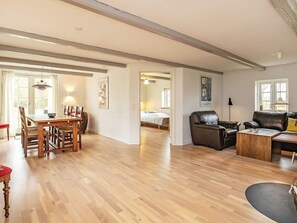 A spacious living area with a wooden floor, a dining table with chairs, a sofa, and a bed in the background. - 8 Person Holiday Home in Fur (Fur)