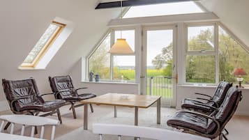 Una habitación con techo inclinado, ventanas grandes y una mesa con sillas.