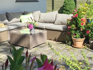 A wicker sofa with cushions, a glass-top coffee table, and a potted plant with pink flowers. - Holiday Home in DronningmÃ¸lle (Dronningmolle)
