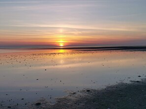 A beach at sunset with calm water reflecting the sky.